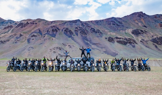 Group of bikers with motorcycles during a Ladakh bike trip, posing against a backdrop of rugged mountains and open skies.