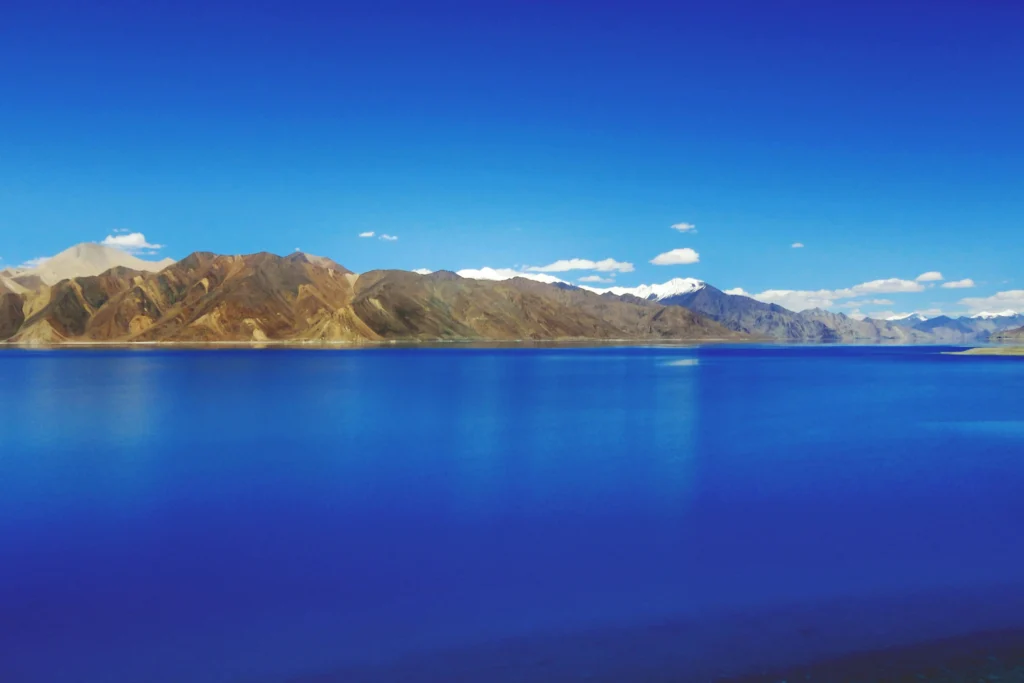 Crystal-clear blue waters of Pangong Lake surrounded by mountains during summer.